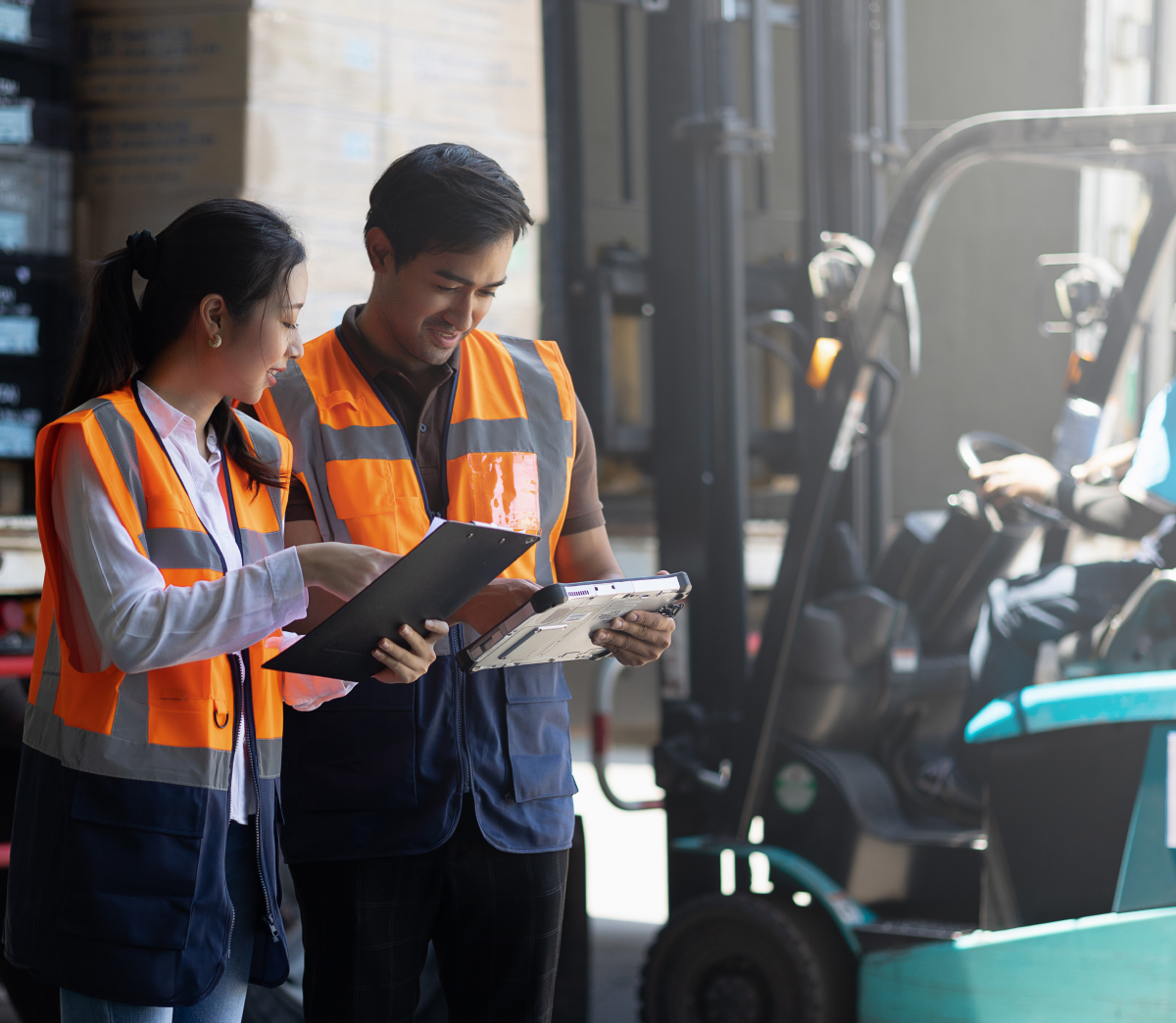 Two workers with a clipboard beside a forklift in a warehouse.