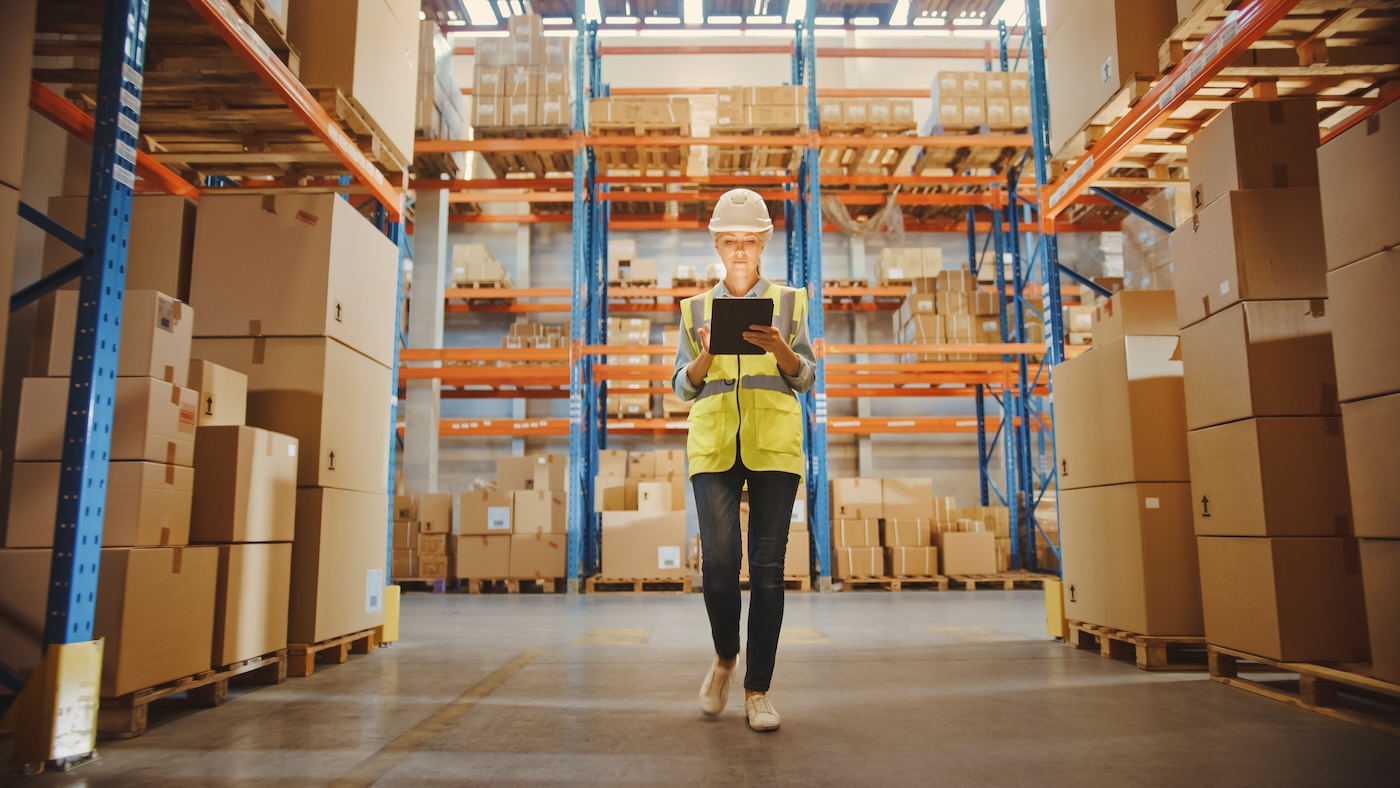 Female Worker Wearing Hard Hat Checks Stock and Inventory with Digital Tablet 